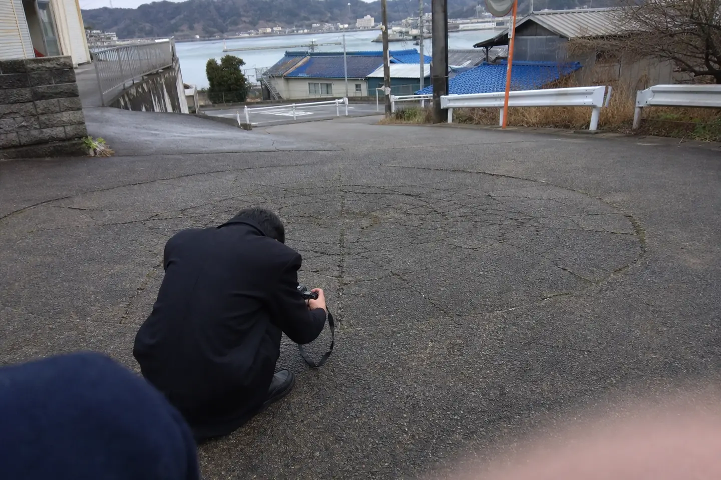 海沿いの古い転回場で、地面すれすれから舗装を撮る少年の後ろ姿