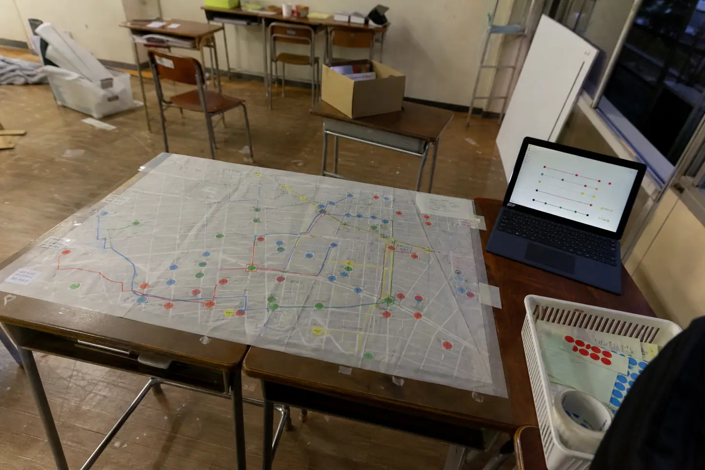 文化祭終了後の教室で、色分けした経路と丸印を重ねた透明地図と展示画面を記録した写真