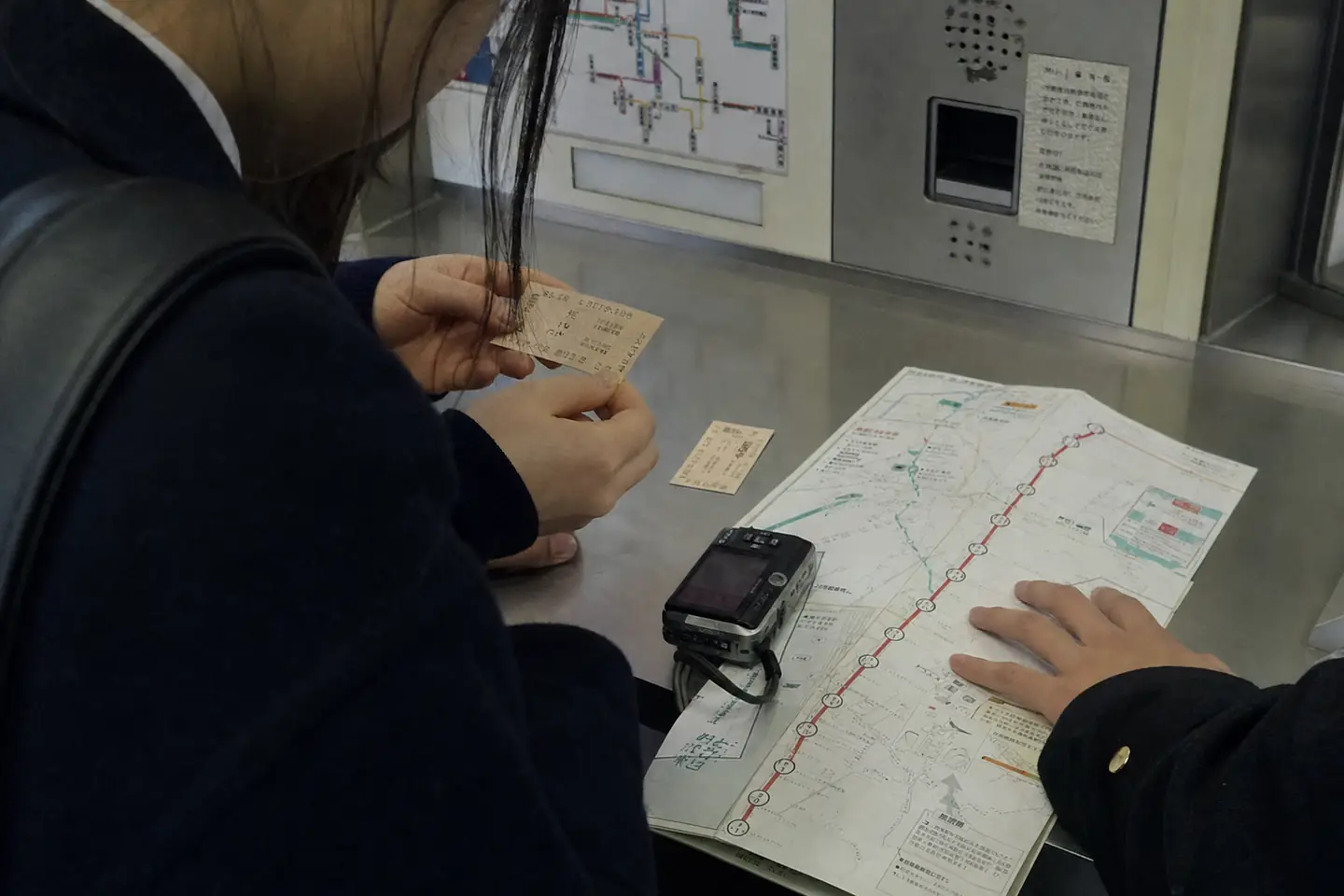 駅の券売機前で、少女が二枚の乗車券の向きを直し、少年が十三駅の地図を押さえる様子